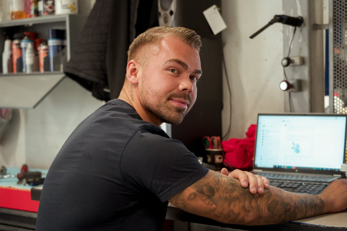 Mann sitter i et bilverksted foran en laptop
